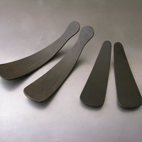 Four sleek, black Ebonized Oak Salad Tossers by Peterman—two long and two short—are neatly arranged on a gray surface, making a stylish dining accessory.