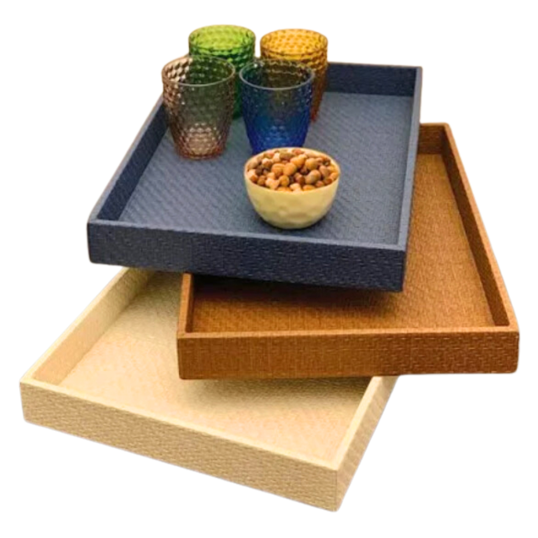Three Bodrum Wicker Rectangle Trays in black are stacked. The top tray holds four colorful textured glasses and a small bowl of nuts. All trays are phthalate-free, ensuring safe and stylish entertaining.