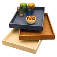 Three Bodrum Wicker Rectangle Trays in black are stacked. The top tray holds four colorful textured glasses and a small bowl of nuts. All trays are phthalate-free, ensuring safe and stylish entertaining.