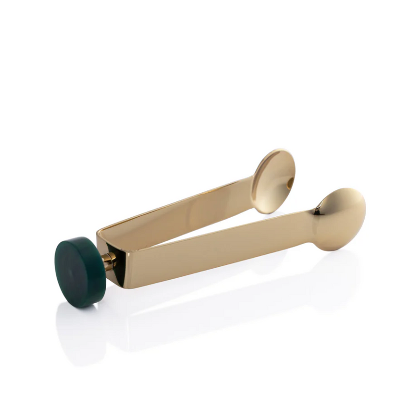 A pair of Spector Ice Tongs by Zodax, featuring a gold metal finish and a flat round green handle, lies on its side on a white surface, reflecting a bit of light.