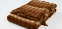 The Mantas Ezcaray Mia Throw, crafted in Europe, features a brown and beige checked wool pattern with fringed edges and is displayed folded on a white surface.