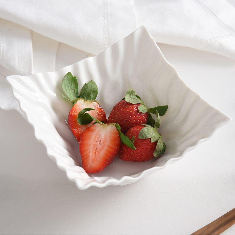 A close-up shows four strawberries, one sliced, resting in a white PAMPA BAY Mascali Snack Bowl Square with a textured rim.