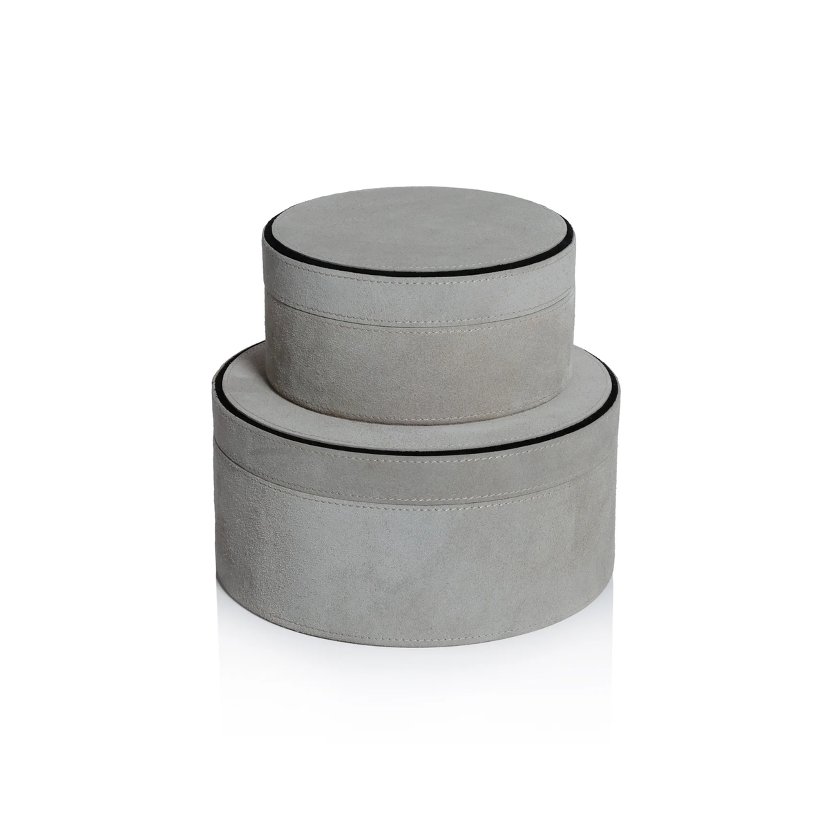 Two round Aldo Suede Box Grey decorative boxes by Zodax are stacked, with the smaller on top. Both feature light gray suede leather and black-trimmed edges, creating a minimalist storage set against a white background.