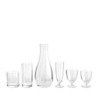 Six mouth-blown glassware pieces from L'Objet's Iris Drinkware Collection—a short tumbler, tall tumbler, wide carafe (center), tall goblet, medium goblet, and small goblet—are displayed in a row against a white background.