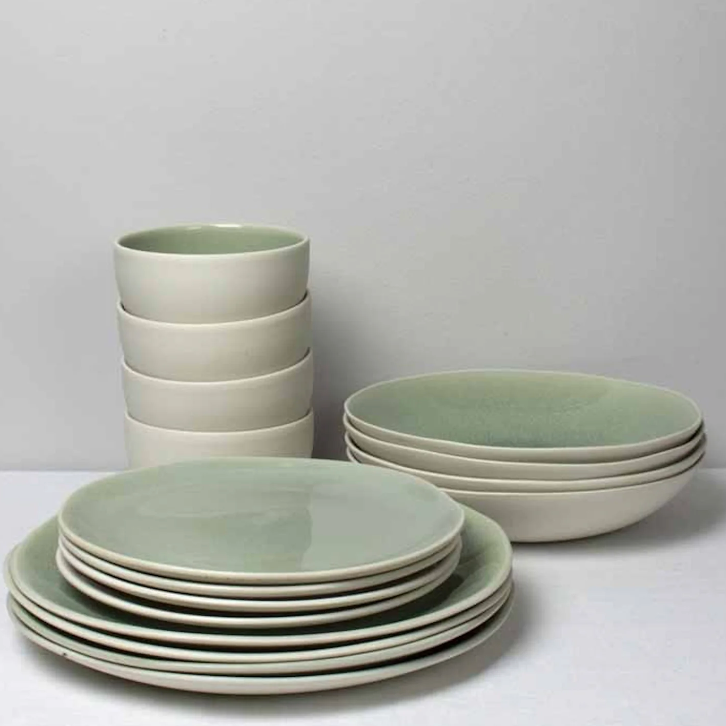 The Maguelone Cachemire Dinnerware by Jars - Rosenthal features stacked plates, bowls, and small cups in soft green and cream hues, arranged neatly on a white surface against a light gray background.
