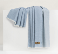 A light blue Aspen Reversible Throw by Lands Downunder with frayed edges is draped over a white surface. A small brown logo tag adds elegance to the soft, cozy blanket.