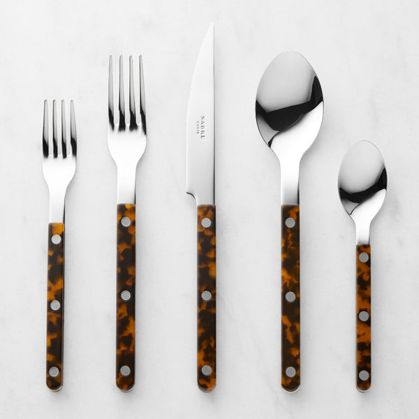 The Sabre Bistrot Flatware 5 Piece Setting-Tortoise—dishwasher safe cutlery with brown tortoiseshell-patterned handles—is arranged side by side on a white marble surface.