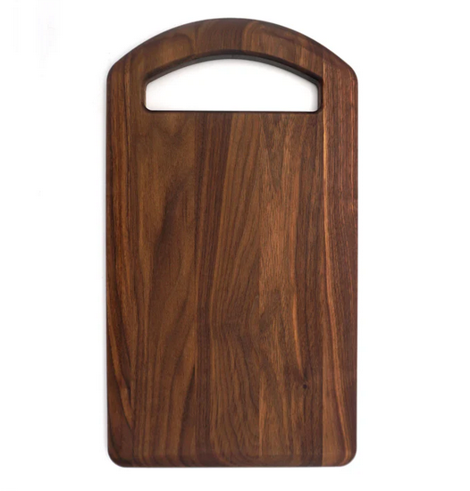 The Bristal Walnut Serving Board by JK Adams features a rectangular shape with a rounded top, arched handle cutout, and showcases a rich, dark walnut grain.