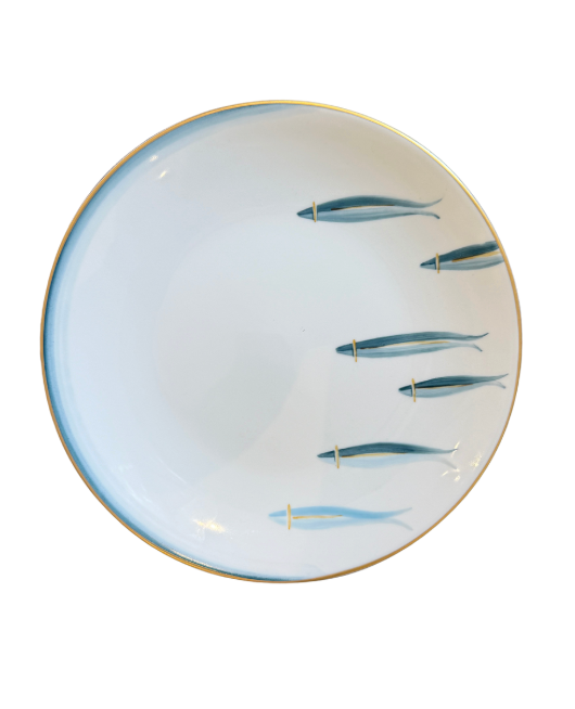 The Marie Daâge Mer d'iroise 1 Dinnerware is a round white ceramic plate with a gold rim and six blue fish in two rows on the right, plus a subtle blue gradient along the left—an elegant design inspired by Limoges porcelain.