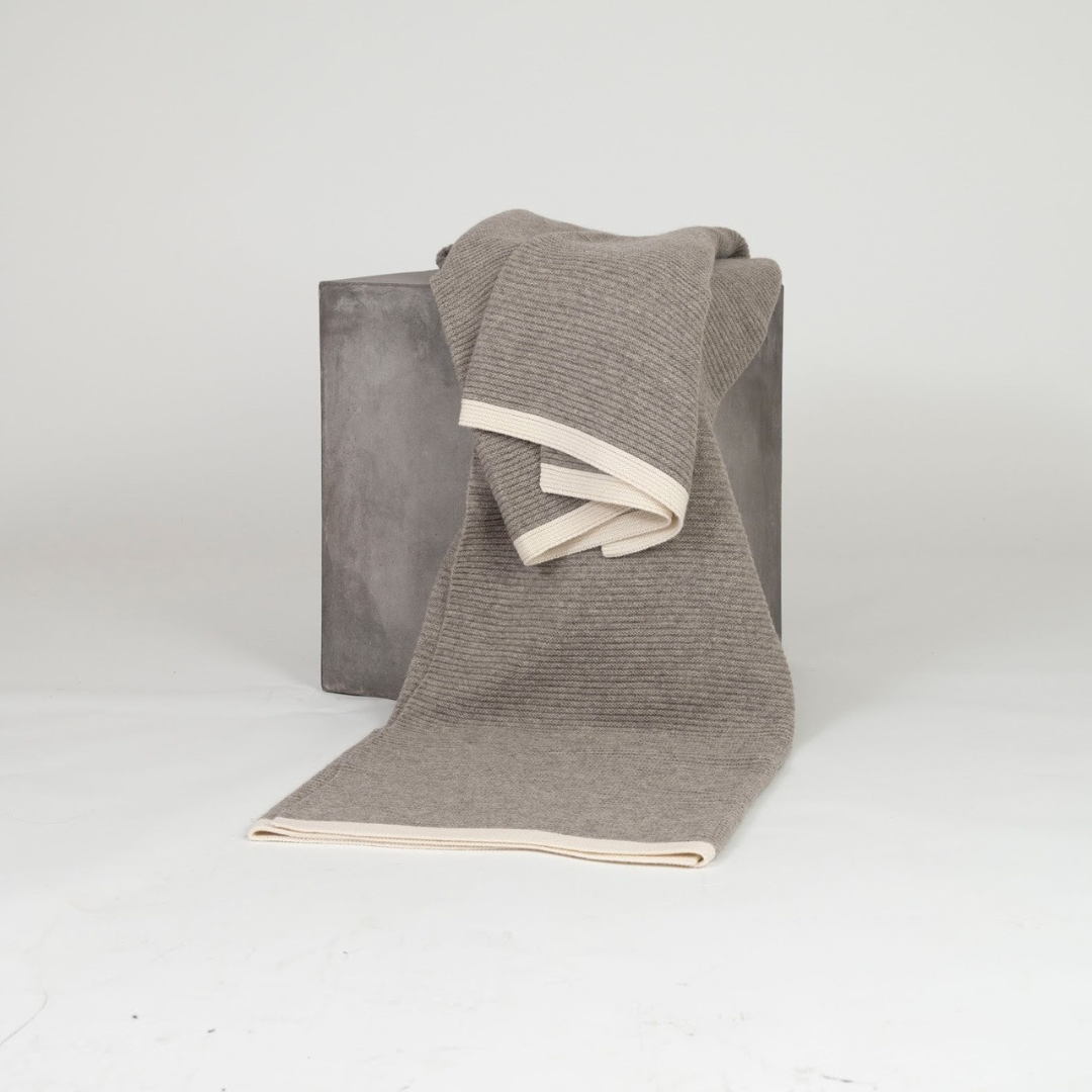 Hangai Mountain Textiles Yak Ribbed Platinum & White Throw in gray with a cream-colored border, draped over a gray cube.