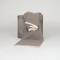 Hangai Mountain Textiles Yak Ribbed Platinum & White Throw in gray with a cream-colored border, draped over a gray cube.