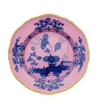 The Ginori 1735 Oriente Italiano Dinnerware Azalea plate features a scalloped edge, pink background, and detailed blue floral motifs inspired by chinoiserie, finished with a thin yellow rim.