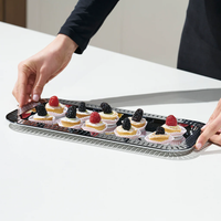 A person places six fruit-topped pastries, each with a raspberry or blackberry garnish, on the Striations Silver Small Rectangle Serving Tray by Anna New York, set on a white surface.