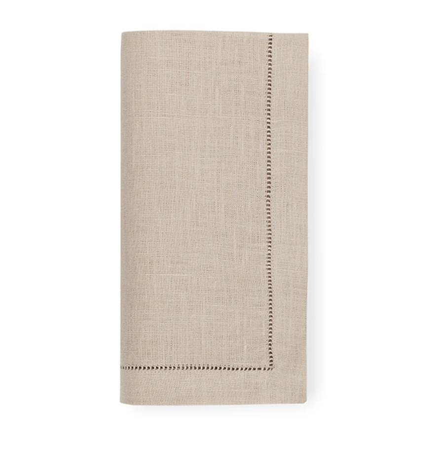 A set of four beige Festival Napkins by Sferra, crafted from fine European linen with a decorative hemstitch border, neatly folded and shown against a white background.