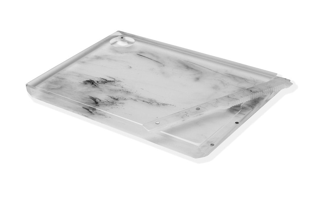 The Apeloig Solid Acrylic Challah Board & Knife is a modern, rectangular white marble-patterned acrylic board with clear edges, a matching clear lid, and a round cutout handle for easy carrying. Set against a white background.