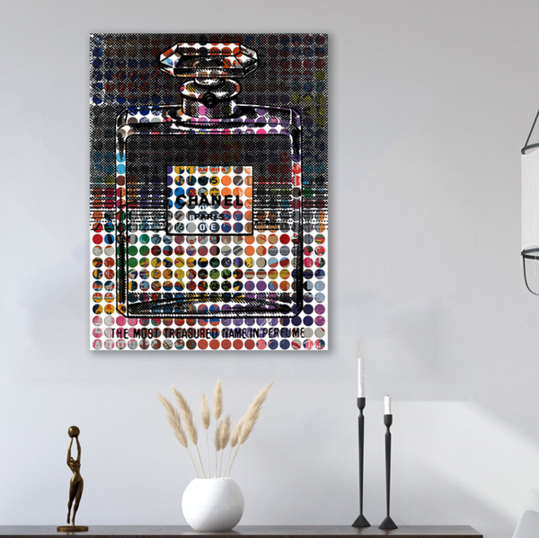 Vintage Chanel Art by Sabeena Jindal, featuring a colorful Chanel No. 5 perfume bottle with circular patterns, hangs above minimalist decor—a white vase with dried grass and two candlesticks—on a white wall.