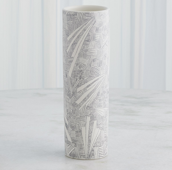The Global Views/Surya Searchlight Vase, a tall cylindrical white piece with abstract black geometric and leaf-like designs, stands on a light surface against a softly striped background.