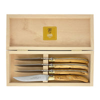 A wooden box houses the Laguiole Steak Knives Set of 4 by Claude Dozorme, each handcrafted knife boasting polished wooden handles arranged meticulously inside. The lid features a gold label adorned with the Claude Dozorme logo and text, reflecting the refined elegance of French cutlery.