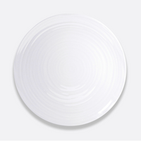 A round, white Bernardaud Origine Dinnerware plate made from fine Limoges porcelain displays subtle concentric ridges, shown from above on a plain light gray background.