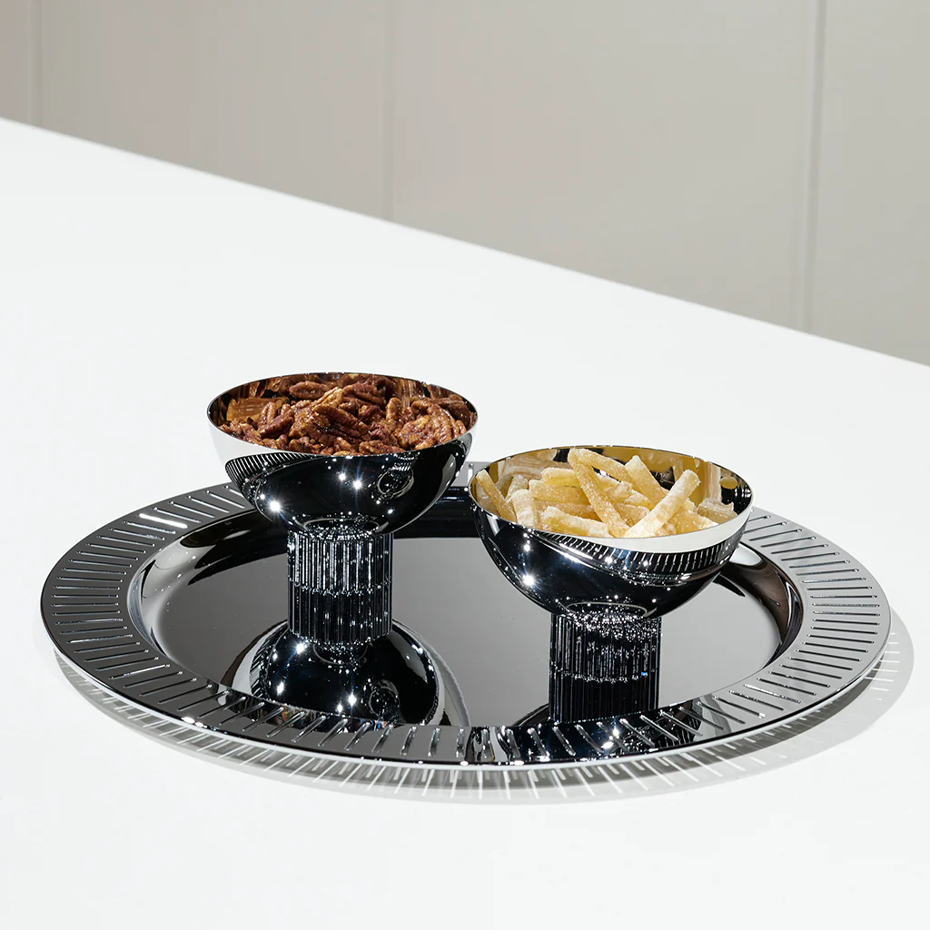 The Anna New York Striations Silver Round Serving Tray displays two metallic pedestal bowls with pecans and potato chips on a white countertop against a neutral background.