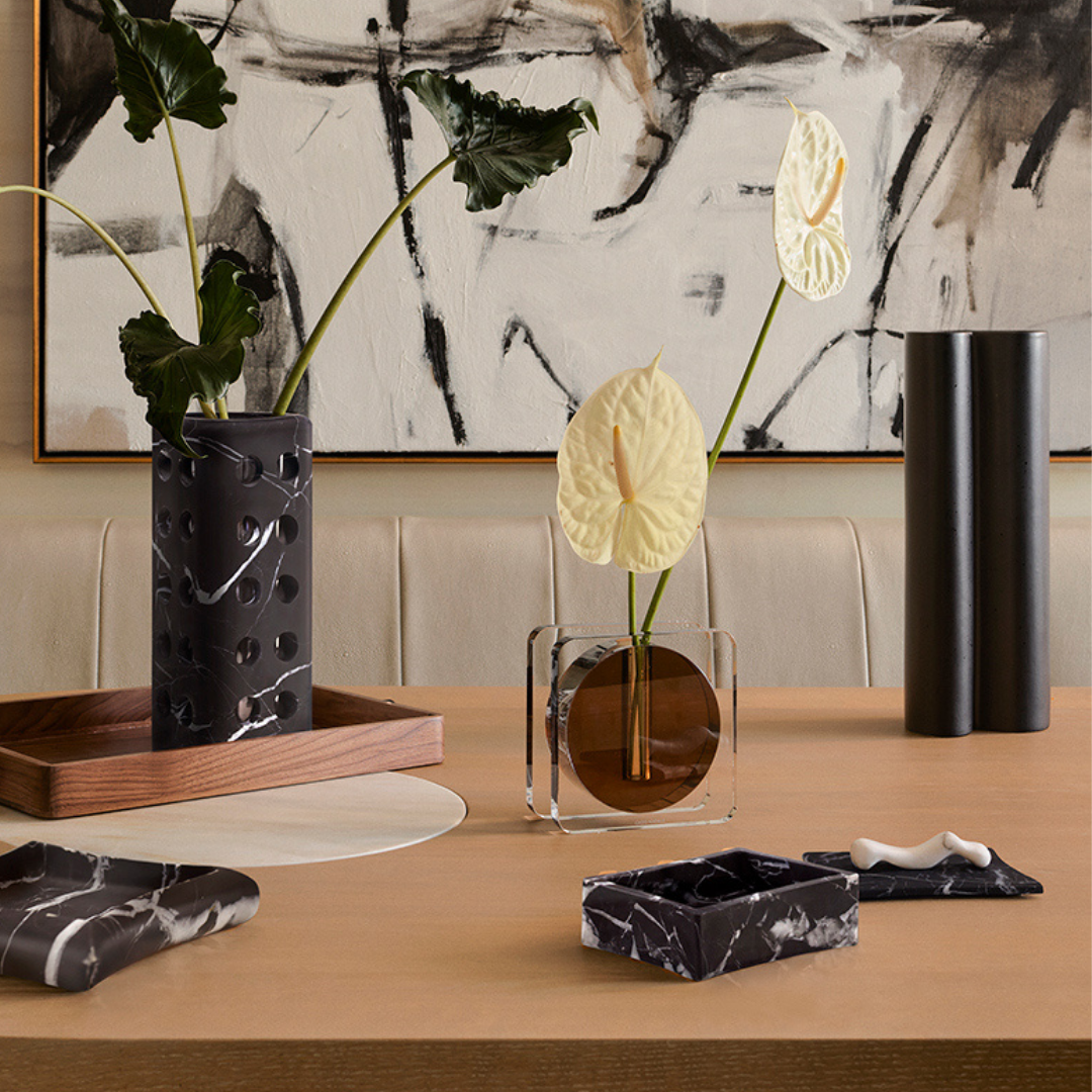 The Caldera Crystal Vase - Clear & Umber by Greg Natale, with its marble-inspired design, adds a decorative touch when displayed on a wooden table alongside sculptural objects and stem vases.