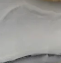 A close-up of a smooth, white frosted surface with gentle swirls, displayed on the Eye Candy Bagel Tray made from food safe silver marble acrylic.