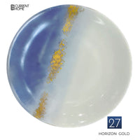 The Marie Daâge Horizon Gold Dinnerware plate is round porcelain, hand-painted with a blue and white gradient and a diagonal gold accent. It features the Marie Daâge logo in the top left corner.