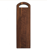 The Bristal Walnut Serving Board by JK Adams features rounded edges, a built-in top handle, and a natural wood grain—ideal as a charcuterie board or stylish serving platter.