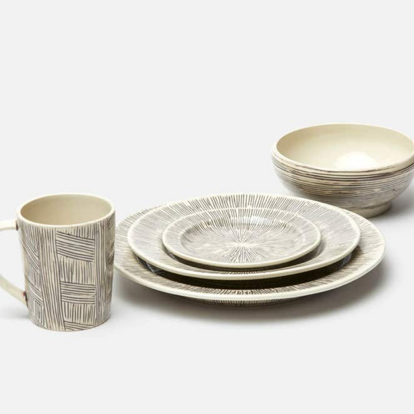 The Nolan Dinnerware Black Cream set by Blue Pheasant includes a mug, two bowls, and three plates with cream bases and linear gray patterns, offering artisanal charm to your tabletop. Each ceramic piece highlights unique handpainted details.