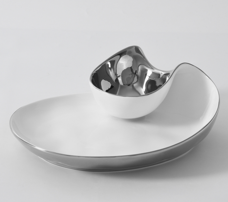 The PAMPA BAY Thin and Simple Chip & Dip is a modern, asymmetrical porcelain platter with a metallic silver rim and attached rounded silver bowl. Oven and dishwasher safe, both pieces have a sleek glossy finish.