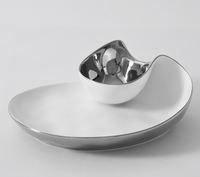 The PAMPA BAY Thin and Simple Chip & Dip is a modern, asymmetrical porcelain platter with a metallic silver rim and attached rounded silver bowl. Oven and dishwasher safe, both pieces have a sleek glossy finish.