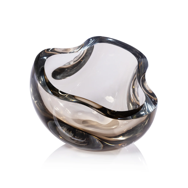 The Zodax Bento Taupe Bowl is a clear, sculptural glass piece with smooth, curved edges and a smoky taupe tint. This elegant bowl is shown against a white background.