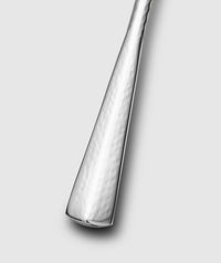 A close-up of the Mary Jurek Alta Slotted Serving Spoon handle highlights its hammered, textured finish against a light gray background—an elegant upgrade to your stainless steel serveware.