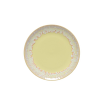 The Costa Nova Taoromina Dinnerware Yellow is a round ceramic plate with a pale yellow center and a wavy pink and white rim, highlighting artisanal craftsmanship. This contemporary piece is displayed on a plain white background.