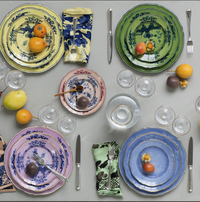 A table set with Ginori 1735 Oriente Italiano Dinnerware in Citrino, paired with matching napkins, silver cutlery, glassware, and small fruits—evoking the vibrant charm of Italian porcelain.