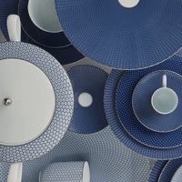 Raynaud's Tresor Dinnerware Blue features elegant blue and white plates, dishes, and teacups with geometric patterns, artistically arranged for a visually striking, textured display.