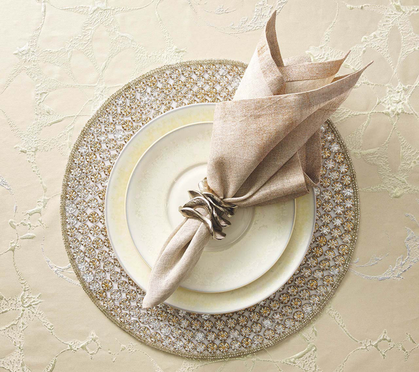 Elegant table decor with a Kim Seybert patterned gold charger, fine china, and a tan napkin held by Kim Seybert Flux Napkin Ring Silver Set of 4 on a cream and gold textured tablecloth.