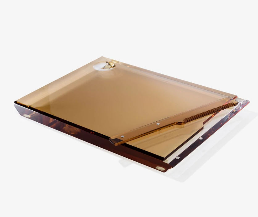 The Apeloig Personalized Solid Acrylic Challah Board is transparent and amber-colored with rounded edges and a gold metal clip, displayed flat on a white surface.