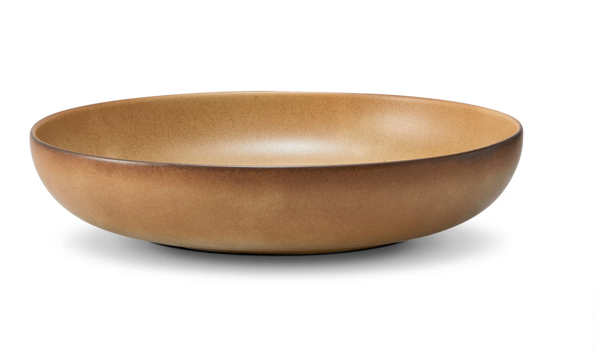 The Terra Leather Dinnerware by L'Objet is a wide, shallow, round ceramic bowl with a smooth matte brown finish, elegantly hand-crafted and displayed on a white background.