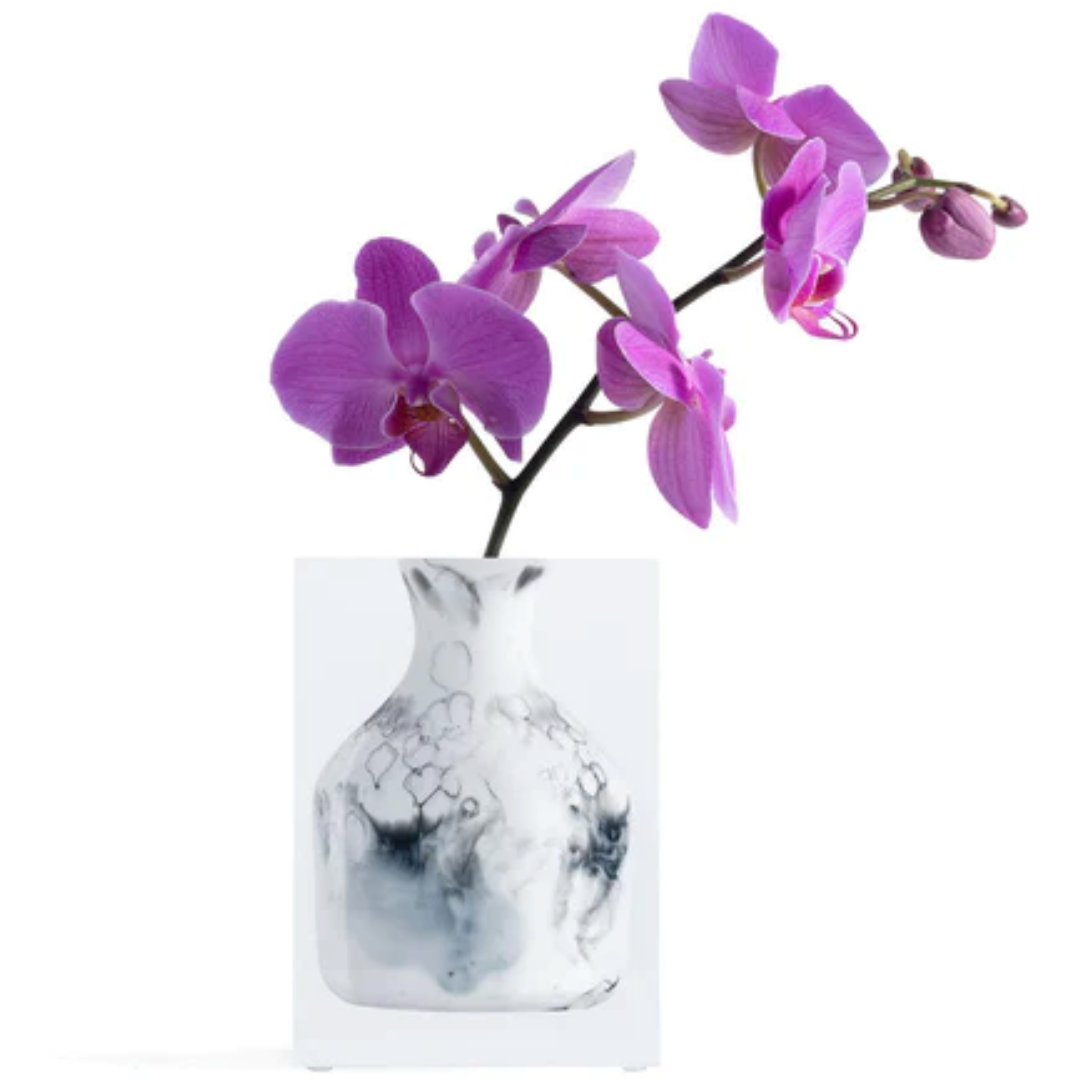 A vibrant purple orchid with several blooms and buds is arranged in a JR William Lucite Vase from the Lucite Vase Collection, featuring black marble patterns, set against a plain white background.