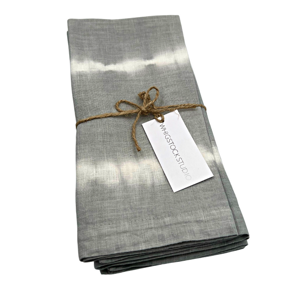 A set of four hand-dyed gray linen napkins from Whigstock Studio, tied with brown twine and a “Whigstock Studio” tag—an elegant, eco-friendly addition to your sustainable essentials collection.