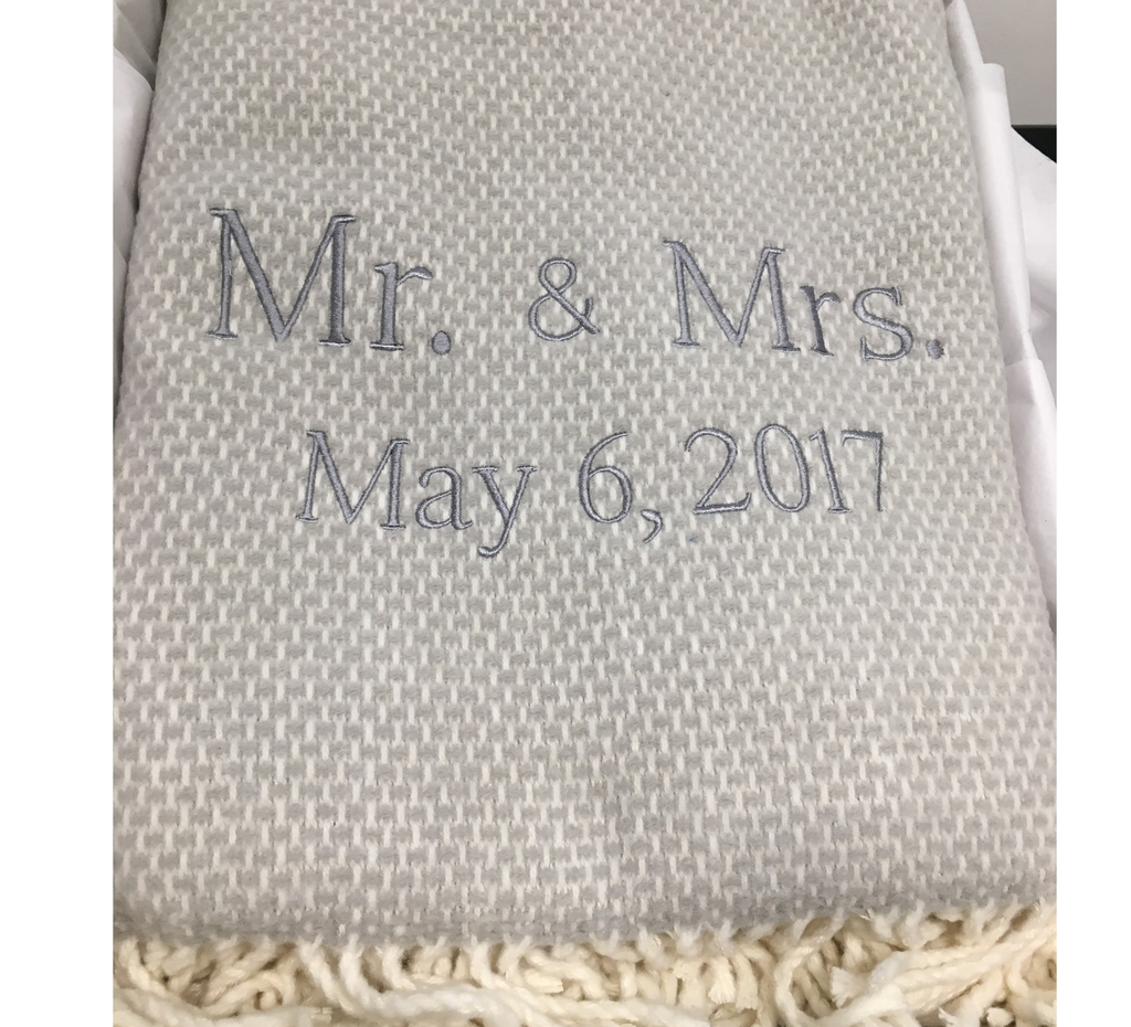 A Soft Idea’s Personalized Throw Blanket is a light gray woven throw with white fringe, embroidered in gray thread with "Mr. & Mrs." and "May 6, 2017," and is neatly folded in a box.