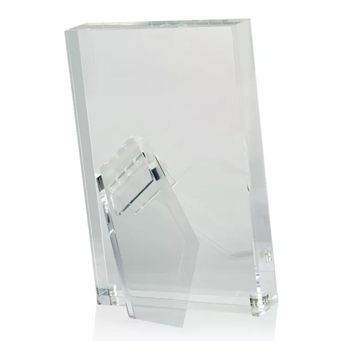 The Tizo Lucite Clear Frame is a minimalist, rectangular acrylic picture frame with a transparent support stand, allowing it to stand upright on flat surfaces. The empty frame is displayed against a white background.