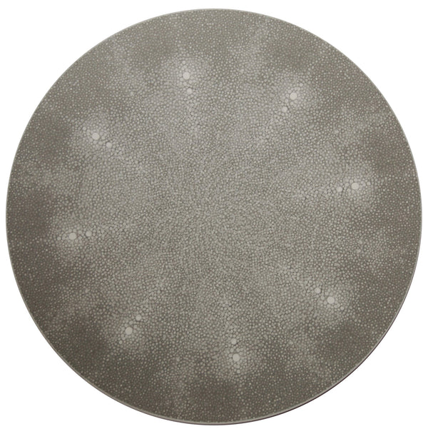 The Shagreen Placemat by Tisch New York features a round, flat, gray design with a subtle textured pattern of small interconnected dots and faint radiating lines that create a starburst effect from the center.