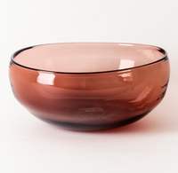 A translucent, round glass bowl in warm rose by Gary Bodker sits on a white background—part of the hand-blown Nesting Bowls Rose stacking set.