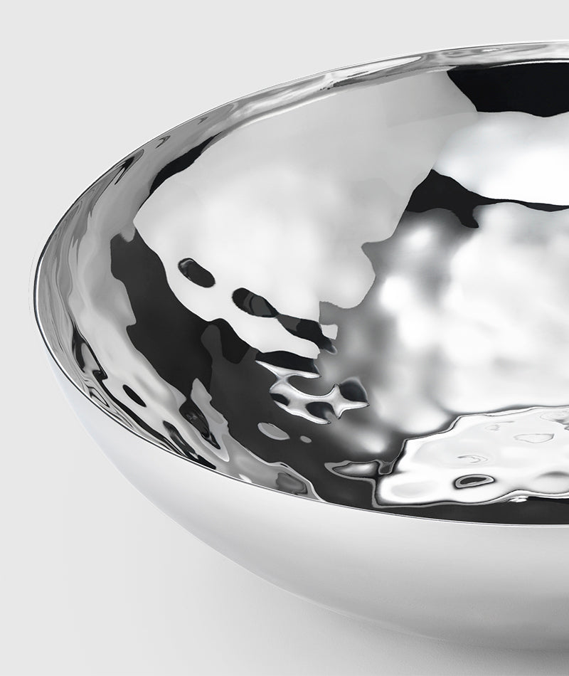 Close-up of the Mary Jurek Luna Serving Bowl 8"—a shiny, reflective stainless steel bowl featuring a smooth curved edge and rippled texture, set against a plain light gray background.