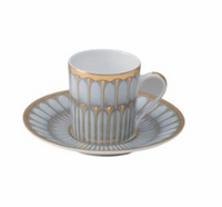 A white porcelain cup and saucer set from Philippe Deshoulieres' Arcades Gold Dinnerware, showcasing gold and gray geometric patterns with gold-accented rims.