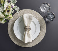 Create an elegant table setting with the Kim Seybert Star Spray Napkin White & Gold & Silver Set of 4, paired with a white plate on a silver charger, gold napkin ring, faceted glasses, and a floral arrangement on a dark surface.