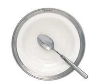 A round, white MATCH Convivio bowl with a metallic rim and hallmark symbols, viewed from above on a white background, holds a shiny metal spoon resting inside.