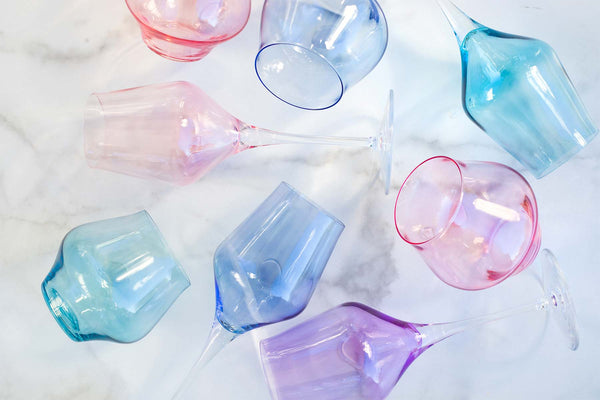 Vietri’s Contessa Stemless Wine Glass Blue and other pastel shades rest on a white marble surface—some upright, others tipped over. These Italian wine glasses are also dishwasher safe.